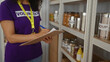 © Krakenimages.com - Woman volunteer writes on clipboard in charity room surrounded by canned goods, emphasizing organization and community service.