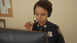 © Krakenimages.com - Woman in police uniform with headset at desk in indoor office setting, focused and attentive while working with equipment and documents in professional environment
