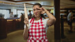 © Krakenimages.com - Woman cook wearing red checkered apron holding a rolling pin and makes v sign to eye in hotel building; playful.