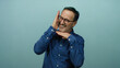 © Krakenimages.com - Hispanic man posing over isolated blue background with a playful expression, capturing a mature, confident aura in a vibrant shirt and glasses.
