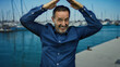 © Krakenimages.com - Hispanic man making gesture at seaside port with boats in the background under a clear blue sky, wearing a blue shirt while standing outdoors on a sunny day.