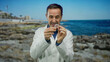 © Krakenimages.com - Mature hispanic man in a lab coat examines dental appliance at the seaside, showcasing thought in an outdoor oceanic setting.