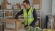 © Krakenimages.com - Mature man in a charity center organizing donations indoors wearing a volunteer vest surrounded by boxes and clothes on racks demonstrating community service involvement