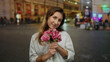 © Krakenimages.com - Young woman holding flowers on bustling city street smiling happily wearing white shirt outdoors urban evening background