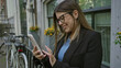 © Krakenimages.com - Woman taking selfie on european street wearing glasses and smiling in black blazer, with bikes and flowers nearby, showcasing urban outdoor setting.