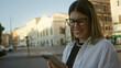 © Krakenimages.com - Young hispanic brunette woman tapping phone screen with both hands on a rome street near historic building, smiling while checking messages; everyday connection contentment.