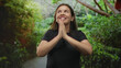 © Krakenimages.com - Young woman with palms pressed together in prayer gesture on forest path among green bushes; gratitude hope.