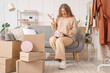 © Pixel-Shot - Young woman with mobile phone unpacking box on sofa at home