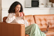 © Pixel-Shot - Beautiful young African-American businesswoman with cup of hot coffee and modern laptop sitting on sofa at home