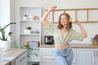© Pixel-Shot - Cool young woman listening to music and dancing in kitchen