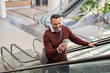 © Rido - Mature businessman on escalator doing video call on mobile phone