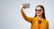 © PRASANNAPIX - Smiling Woman Taking Selfie with Smartphone and Stylish Sunglasses