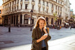 © Davor - Young adult woman smiling at smartphone on historic city street