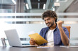 © Tetiana - A young Muslim man is sitting in the office and is happy about the received letter and news, showing a victory gesture with his hand