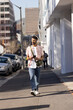 © Wavebreak Media - South Asian man walking on city sidewalk checking smartphone wearing white headphones and green bag