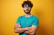 © Viktor - Young man with curly hair, beard, glasses poses confidently. Wears turquoise t-shirt, arms crossed. Guy looks at camera on yellow background. Serious male model, smart student, pro adult, tech worker