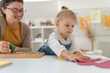 © lordn - Little girl focusing on a craft activity while an adult supports her in a bright, creative home environment