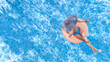 © Iuliia Sokolovska - Aerial drone view of beautiful woman in hat relaxing in swimming pool, young girl in bikini swims on inflatable ring donut and has fun in blue pool water, tropical vacation on holiday resort