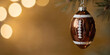 © freedarts - Christmas ornament shaped like a brown football with white lacing, hanging from a spruce branch against a golden background with bokeh lights.