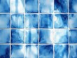 © Milana - Close-up of blue and white ceramic tiles arranged in a grid pattern reflecting light with varying shades of blue
