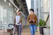© Wavebreak Media - Diverse male friends walking outdoors wearing headphones pushing bicycle holding notebook