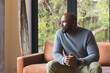 © Wavebreak Media - African American man sitting at home on sofa near glass window and wooden beam checking wristwatch