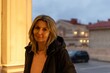 © svetograph - Woman portrait city street at dusk standing by a warmly lit architectural column, smiling casually in winter jacket