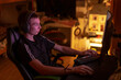 © Viktar - White teen focused at gaming setup, headset on, hands on keyboard and mouse, monitor glow illuminating face, warm ambient lamp and neon accent, ergonomic chair reclined, late night concentration