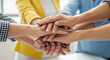 © abu - A diverse group of people stack their hands together symbolizing teamwork and unity in a brightly lit modern business environment showcasing collaboration.