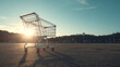 © AndyAziz - Shiny chrome shopping cart standing alone on empty asphalt parking lot with sunset sunlight and shadows