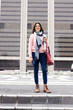 © Wavebreak Media - Senior woman smiling and standing on steps at urban plaza holding coffee cup, smartphone, tote bag