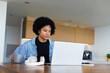 © Wavebreak Media - African American man working on silver laptop at kitchen island while holding grey mug and notebook