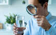 © Aminograpix - Man Inspecting Glass of Water with Magnifying Glass for Quality Check