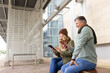© Wavebreak Media - Senior couple sitting on bench under metal canopy at transit platform checking devices, copy space