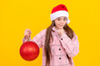 © Olena - thinking teen girl in santa claus hat hold christmas decorative ball on yellow background, santa