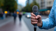 © Curioso.Photography - A handheld microphone pointed toward a blurred city crowd during an outdoor public event.