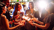 © maxbelchenko - A happy group is having fun at a bar, drinking drinks, and lighting sparklers in a cozy space. Young men and a woman are enjoying celebration and having fun at bar. Concept of party, celebration.