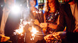 © maxbelchenko - A happy group is having fun at a bar, drinking drinks, and lighting sparklers in a cozy space. Young men and a woman are enjoying celebration and having fun at bar. Concept of party, celebration.