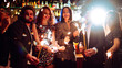 © maxbelchenko - A happy group is having fun at a bar, drinking drinks, and lighting sparklers in a cozy space. Young men and a woman are enjoying celebration and having fun at bar. Concept of party, celebration.