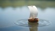 © Nur - A small wooden toy boat with a white sail floats on calm water, creating gentle ripples, with blurred reflections in the background.