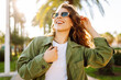 © maxbelchenko - A cheerful woman is enjoying herself in a sunny park. A backpacker wearing sunglasses enjoys a walk among the palm trees. Concepts of relaxation, weekends, and enjoyment.