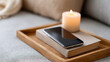 © Anastasiya Marchenko - Cozy home setting with smartphone on closed book and lit candle on wooden tray placed on fabric sofa