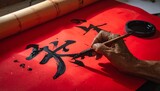 Artist hand painting traditional Chinese calligraphy character for good fortune on red paper.