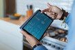 © Wavebreak Media - Tablet showing thermostat and weather being held over counter beside stovetop tools and lemon bowl