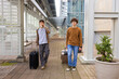 © Wavebreak Media - Two men walking on covered walkway pulling suitcases with backpack sipping paper coffee cup