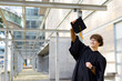 © Wavebreak Media - White male graduate standing under canopy in black gown holding cap overhead smiling, copy space
