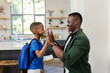 © Wavebreak Media - African American father and child giving high-five at kitchen island with blue backpack and watch