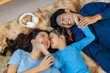 © amnaj - Happy Asian family laughing, cuddling, and lying together on a fluffy rug at home, cherishing moments of warmth and connection