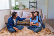 © amnaj - Loving Asian family with parents and daughter playing and laughing in living room at home, sharing bonding time
