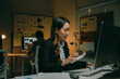 © Crystal - Businesswoman calculating finances at her desk in a dark office, concentrating on her work during overtime. Stressful deadline approaching